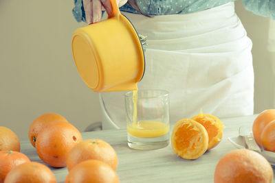 Midsection of woman pouring juice of orange on table