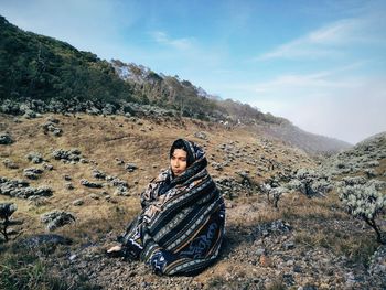 Man sitting on mountain against sky