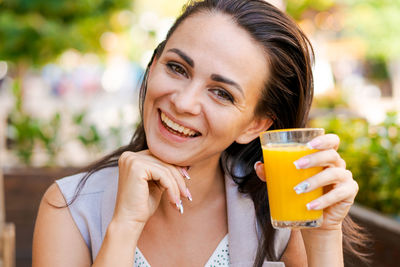 Happy business woman in street cafe drinks natural juice and smiles on sunny day.