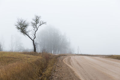 Dirt road amidst field against sky