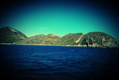 Scenic view of sea and mountains against clear blue sky