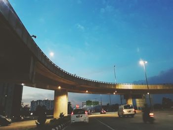 Cars on bridge against sky in city at dusk