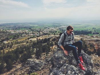 Full length of man sitting on mobile phone against sky