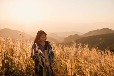 Young woman standing on field against sky during sunset