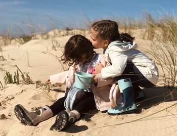 Side view of girls sisters  sitting on sand at beach