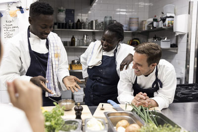 Chef explaining smiling multiracial colleagues at kitchen in restaurant
