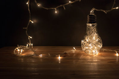 Close-up of fairy lights and light bulb on wooden table against black background