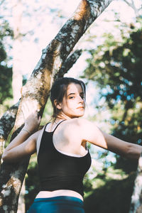 Young woman standing by tree trunk