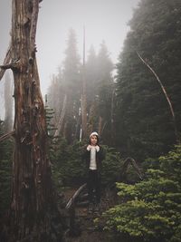 Portrait of young woman standing in forest during foggy weather