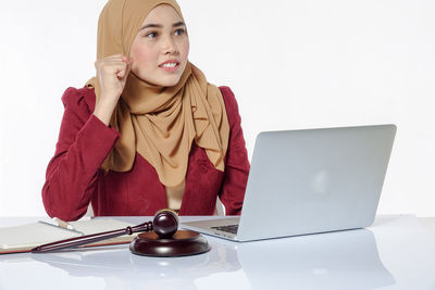 Young businesswoman using laptop while sitting against white background