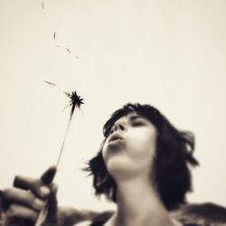 Low angle view of woman blowing on dandelion seeds against sky