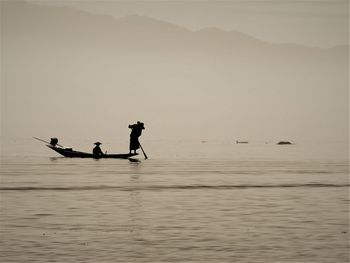 Silhouette people enjoying in sea against sky during sunset