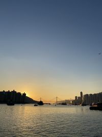 Sea and silhouette buildings against sky during sunset