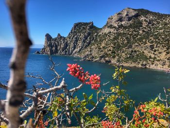 Scenic view of sea by mountain against blue sky