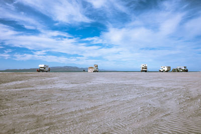 Distant view of travel trailers parked at beach against cloudy sky