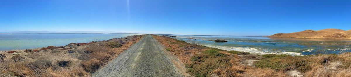 Panoramic view of road against clear blue sky by the water. 