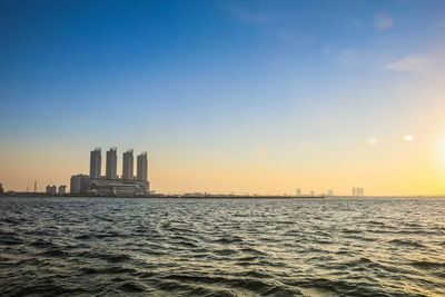 Sea by buildings against sky during sunset