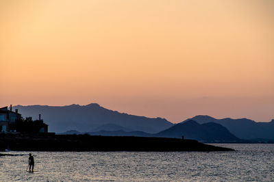 Silhouette mountains by sea against orange sky