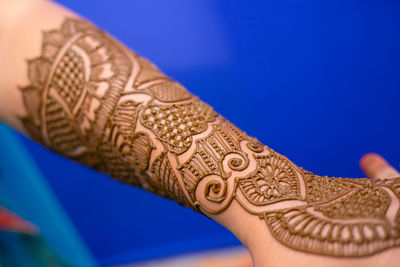 Cropped hand of bride with henna tattoo against blue background