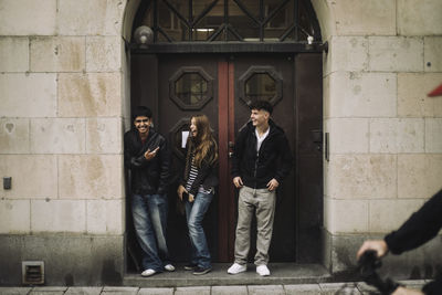 Happy male and female teenage friends laughing while standing near building door