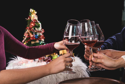 Close-up of friends toasting drinks during christmas celebration against black background