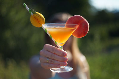 Woman holding orange peach cocktail glass in front of her face