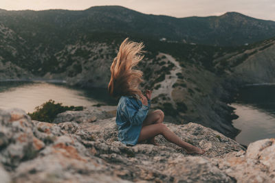 Rear view of woman sitting on rock against mountain