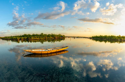 Fishing boat in lake against sky during sunset