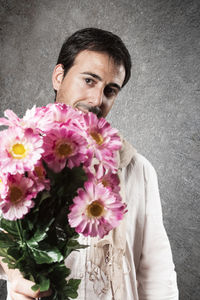 Portrait of man holding pink flowers bouquet while standing against wall