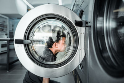 Side view of boy looking at washing machine in laundromat