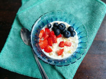 Cooked oat with forest fruits. strawberries and blueberries in a blue glass bowl on a green napkin.
