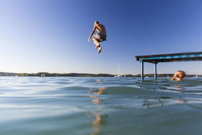 Low angle view of boy jumping into lake against clear blue sky