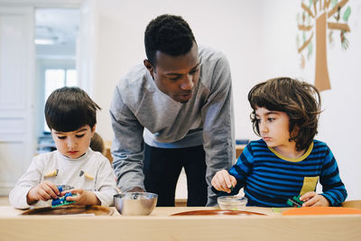 Male teacher looking at students playing with toys at table in child care classroom