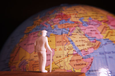 Close-up of figurine on table by globe against black background