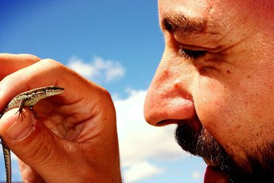 Close-up of man holding lizard against sky