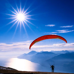 Person paragliding over mountains against sky