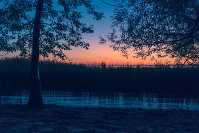 Silhouette trees by lake against sky during sunset