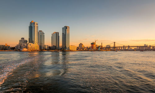 Sea by buildings against sky during sunset