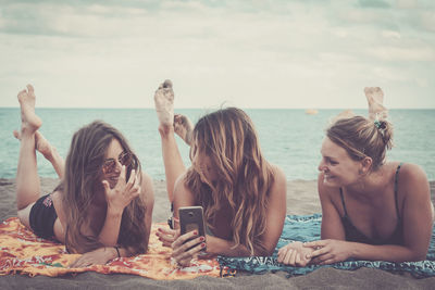 Smiling friends relaxing at beach against sky