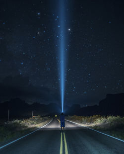 Rear view of man holding flashlight against sky at night