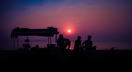 Silhouette people standing by sea against sky during sunset