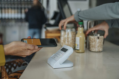 Mature customer with mobile phone paying through bar code scanner in retail store