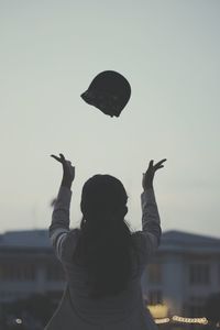 Rear view of woman throwing cap against clear sky