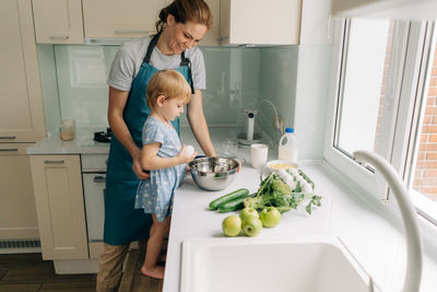 In a large bright kitchen a young mother and little daughter are preparing dinner.