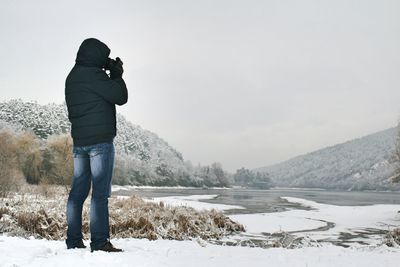 Rear view of woman photographing on snow covered landscape