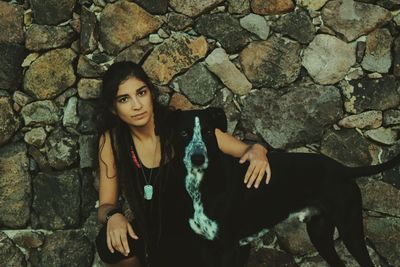 Portrait of confident young woman with dog against stone wall