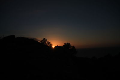 Silhouette trees on landscape against sky at sunset