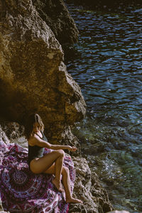 Side view of woman sitting on rock in sea