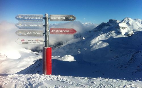 Road sign on snow covered mountain against sky