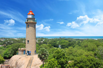 Lighthouse amidst trees and buildings against sky